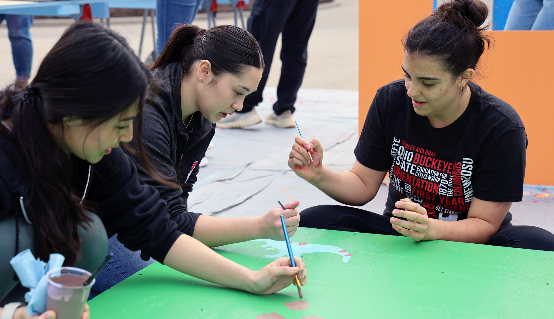 Three public health students paint on a playhouse as part of a service project benefitting a local family.